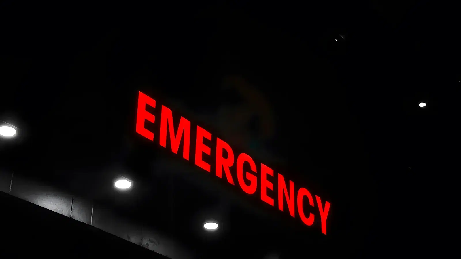 A red illuminated EMERGENCY sign glowing above a hospital entrance in the dark